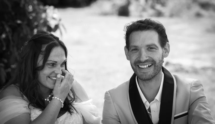 Les mariés sourient, assis côte à côte, en noir et blanc.