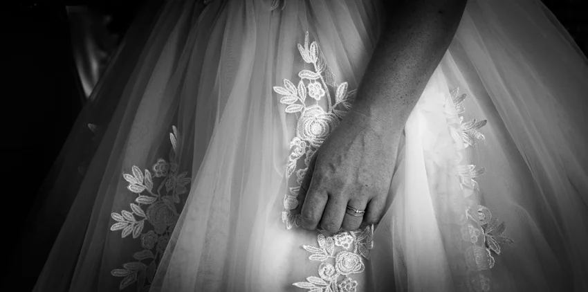 Une main et son alliance sur la dentelle de la robe.
